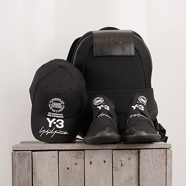 Schwarze Y-3-Kollektion: Basecap, Sneaker und Rucksack auf Holzbank.