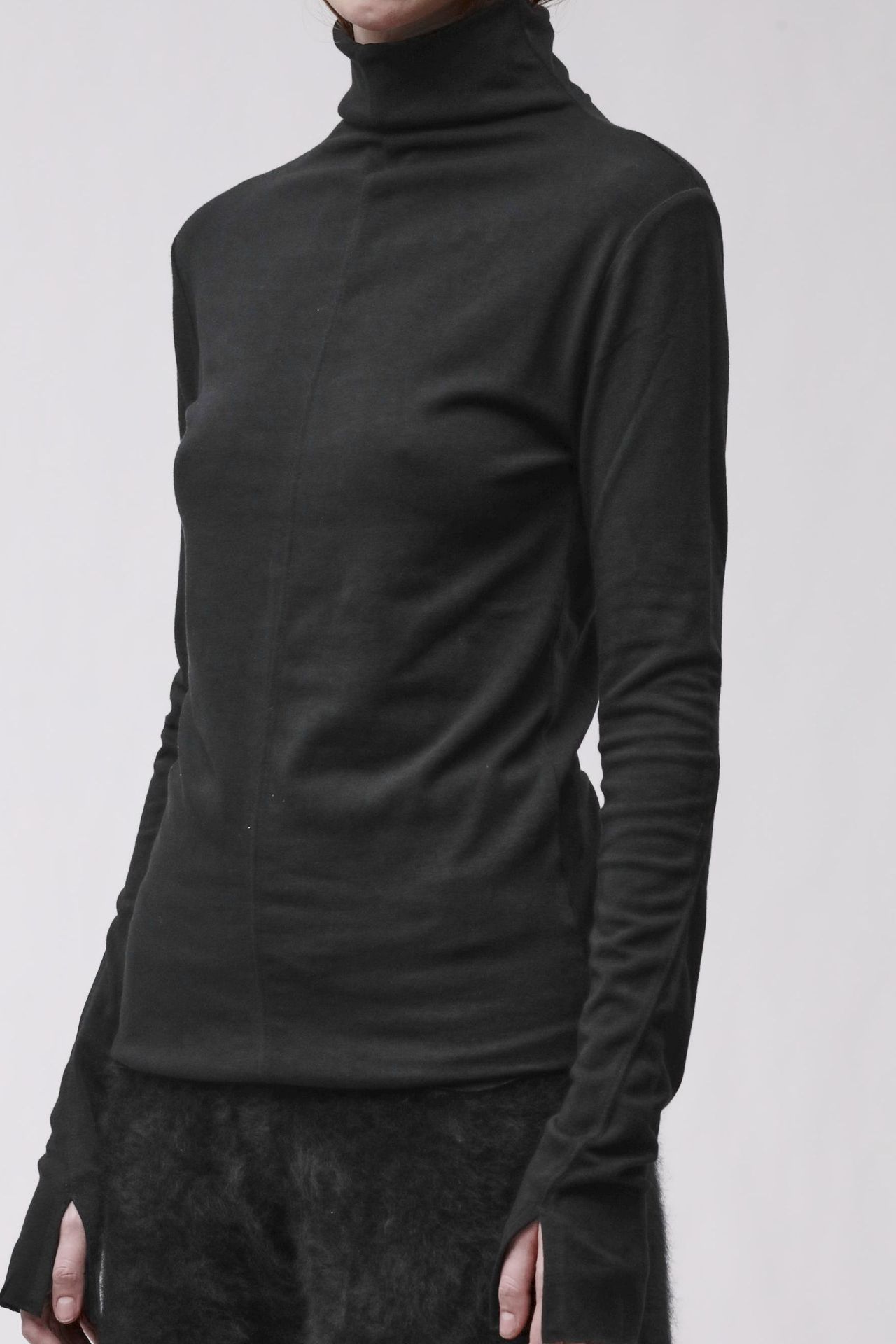 Frau trägt schwarzes Turtleneck-Kleid mit weitem Schnitt und texturierten Hosen, seriös-elegant.