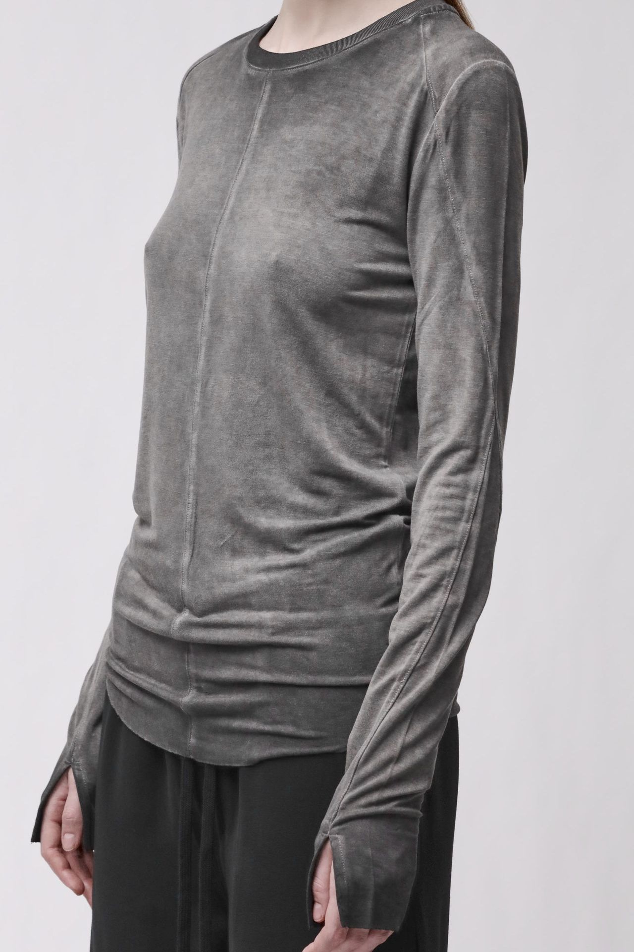 Frau trägt graues langärmliges Shirt und schwarze weite Hose, seriöser Look.