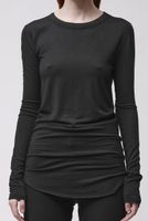Frau trägt schlichtes, langärmliges schwarzes Top mit gerüschtem Saum und schwarze Leggings.