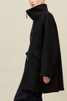 Frau trägt oversized schwarzen Mantel mit weitem Schnitt, dunkle weite Hose und schwarze Schuhe.