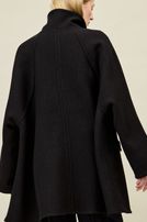 Frau trägt oversized schwarzen Wollmantel mit hochgeschlagenem Kragen, dunkle Jeans.
