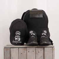 Schwarze Y-3-Kollektion: Basecap, Sneaker und Rucksack auf Holzbank.