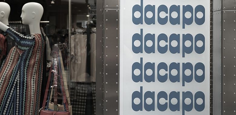 Dacapo-Ladenfront mit Mannequin in gestreifter Jacke und Logo-Wand.