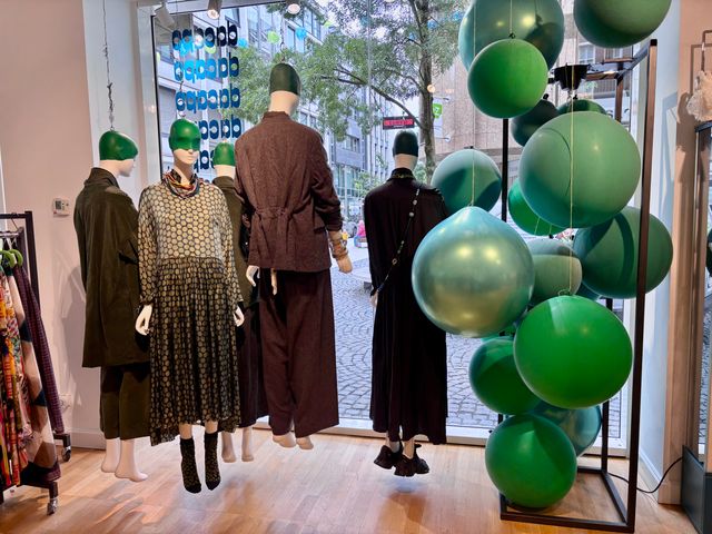 Modenschau mit Mannequins und grünen Ballons vor Stadtkulisse.