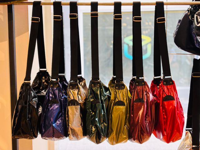 Bunte, glänzende Handtaschen in verschiedenen Farben hängen an Stange zur Schau.
