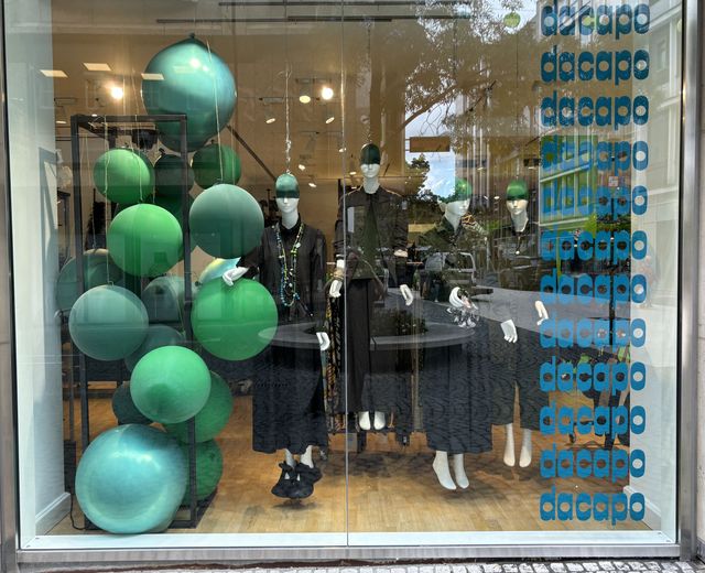 Modisches Schaufenster mit grünen Ballons, Kleidung und Accessoires in elegantem Design.