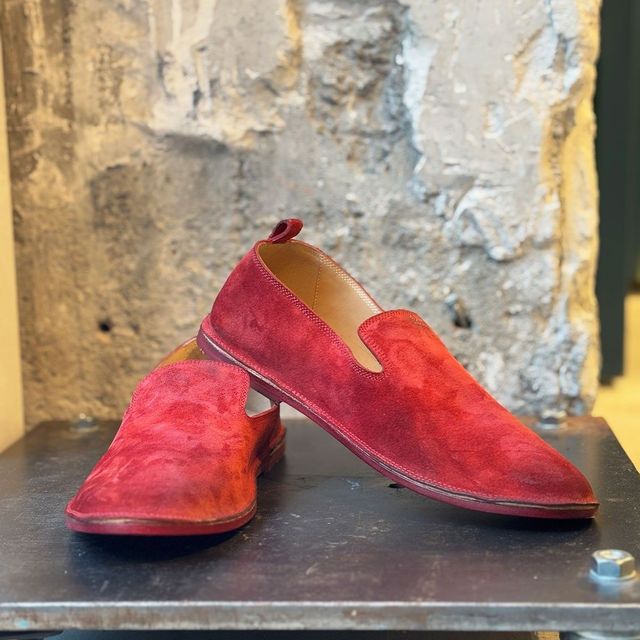 Rote Lederslipper mit Zehenschlitz auf Metalloberfläche vor texturierter Wand.