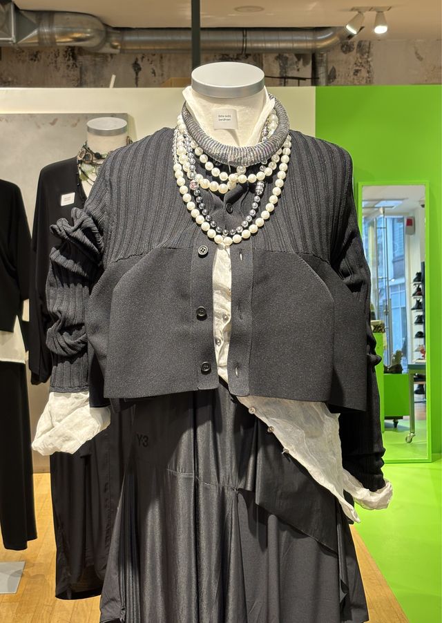 Elegantes Damen-Outfit mit grauer Jacke, schwarzem Kleid und Perlenkette auf Mannequin.