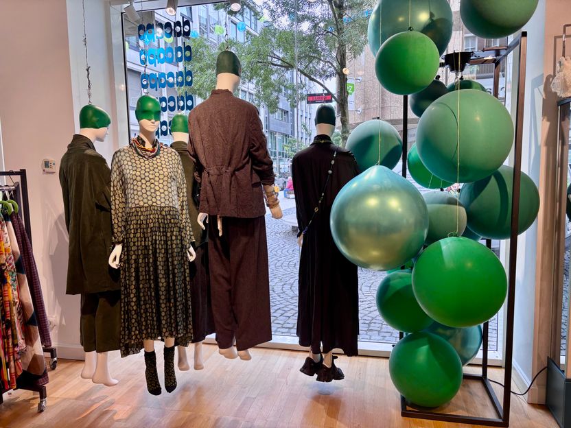 Modenschau mit Mannequins und grünen Ballons vor Stadtkulisse.