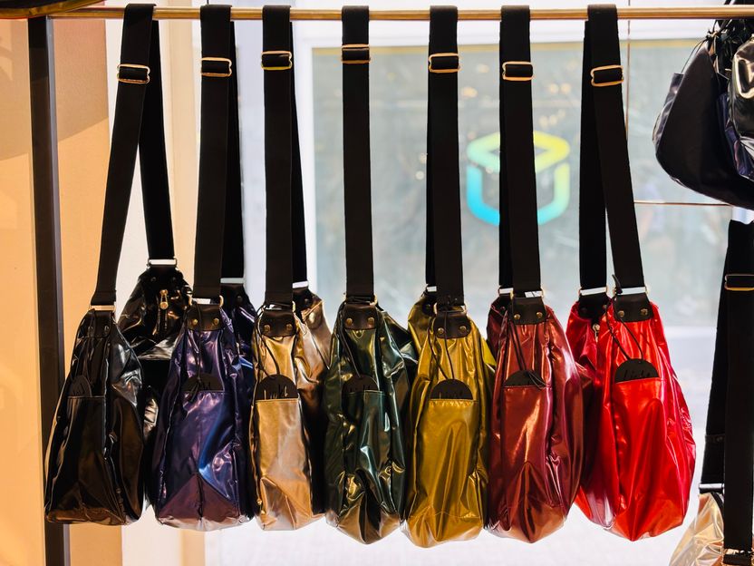 Bunte, glänzende Handtaschen in verschiedenen Farben hängen an Stange zur Schau.