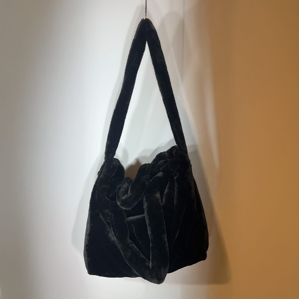 Schwarze Samttasche mit Fransen und strukturierter Stickerei an der Wand hängend.