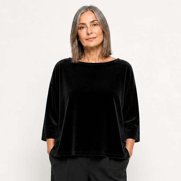 Frau trägt elegantes schwarzes Velours-Top mit weitem Schnitt und weite schwarze Hosen, schlichtes Styling.