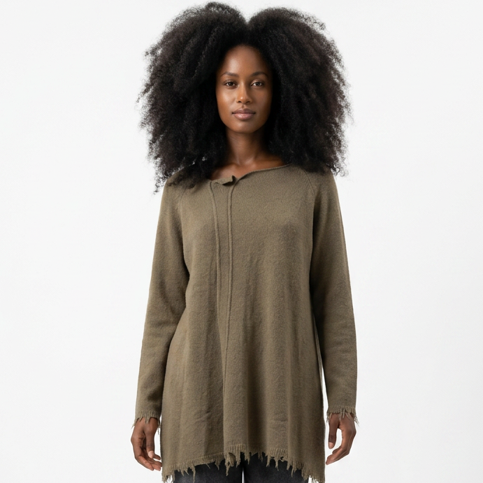 Person trägt olivfarbenen oversized Pullover mit Fransen, graue weite Hose und weiße Sneaker.