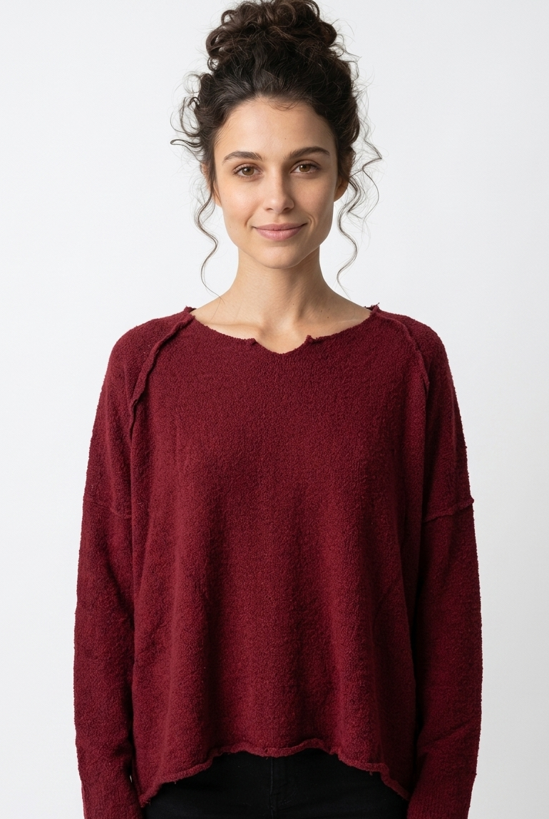 Frau trägt burgunderfarbenen oversized Pullover mit hochgestecktem Haar, lächelt freundlich.