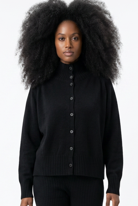 Schwarzer oversized Pullover mit Knopfleiste, weite Hose und flache Schuhe, Person mit voluminösen Locken.