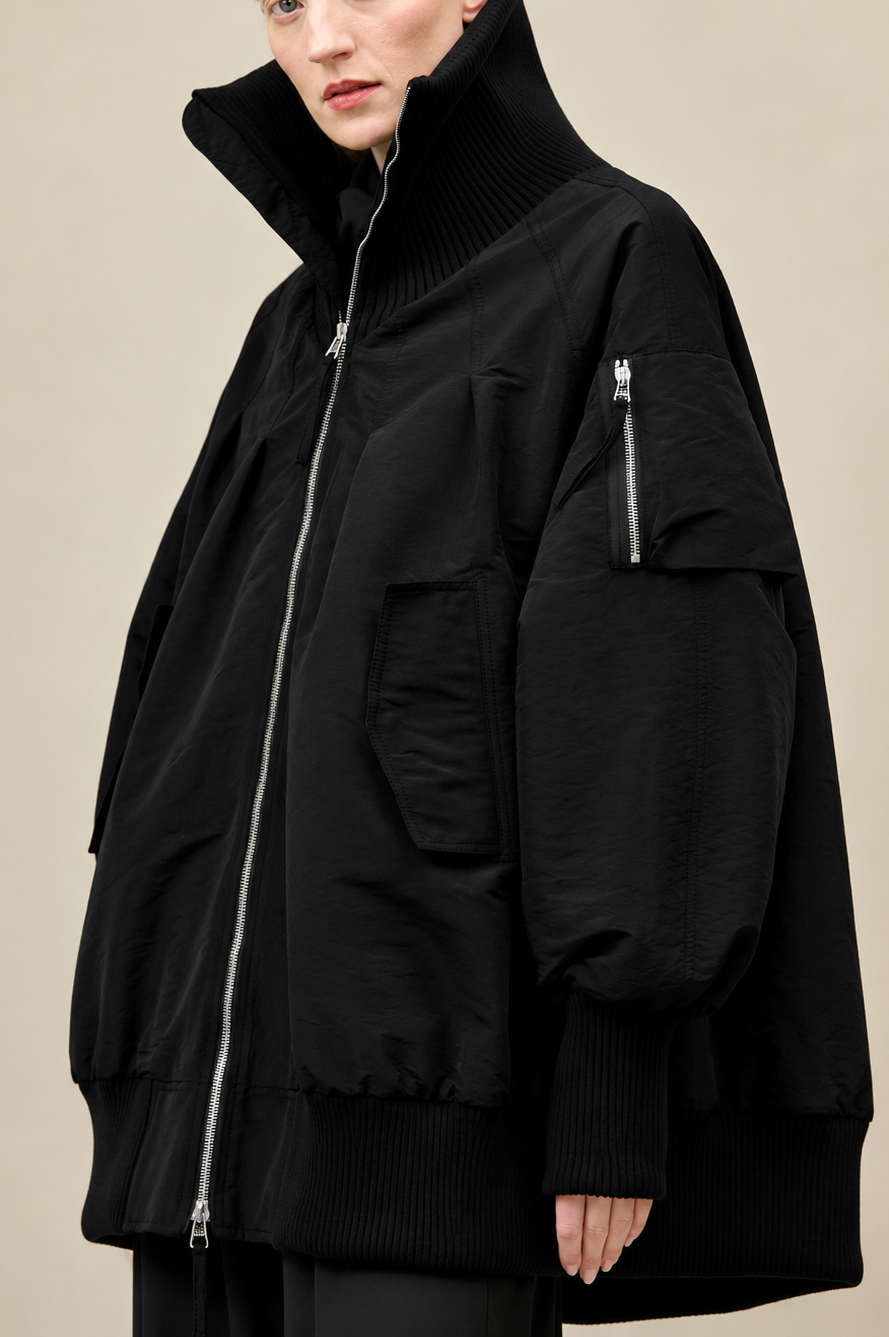 Schwarzer oversized Mantel mit hochgeschlagenem Kragen und Zipper-Pockets, elegant und modern.
