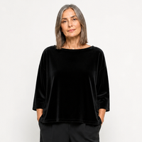 Frau trägt elegantes schwarzes Velours-Top mit weitem Schnitt und weite schwarze Hosen, schlichtes Styling.