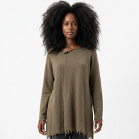 Person trägt olivfarbenen oversized Pullover mit Fransen, graue weite Hose und weiße Sneaker.
