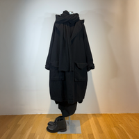 Schwarzer oversized Mantel mit Pelzkragen auf Mannequin mit schwarzen Schuhen.