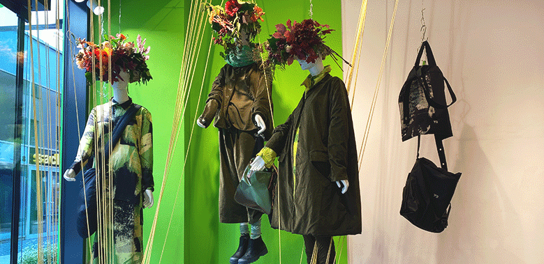 Modische Herbstkollektion mit Mannequins und Accessoires in grüner Vitrine.
