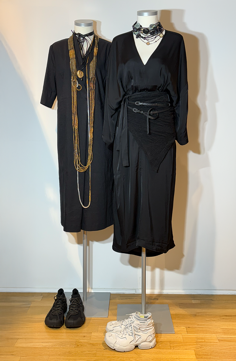 Zwei elegante schwarze Kleider mit Accessoires und passendem Schuhwerk auf Mannequins.
