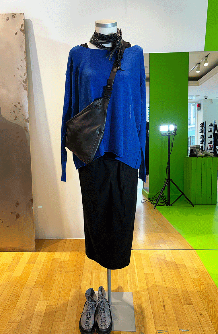 Modell auf Mannequin mit blauem Sweatshirt, schwarzem Rock, Tasche und Schuhen in Ausstellungsvitrine.