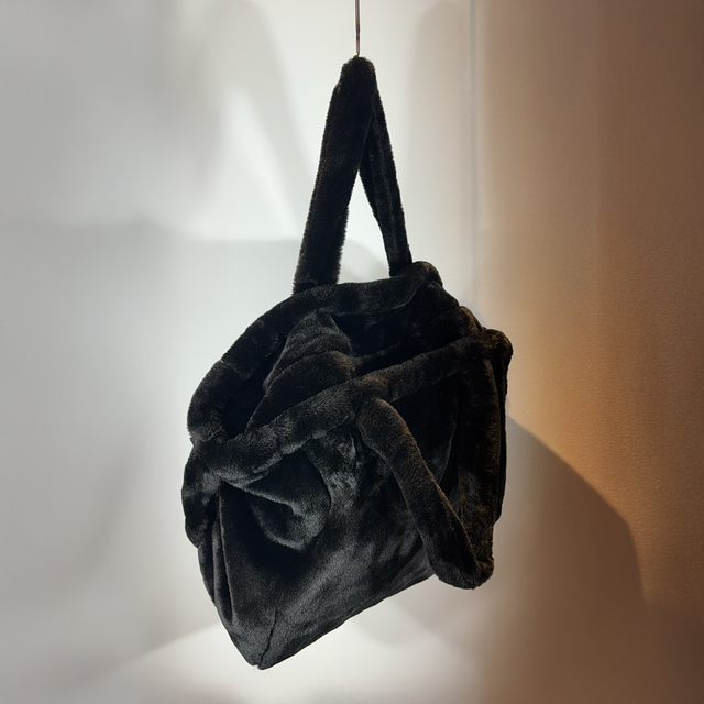 Schwarze, flauschige Handtasche mit zwei Henkeln, hängend an Wand.