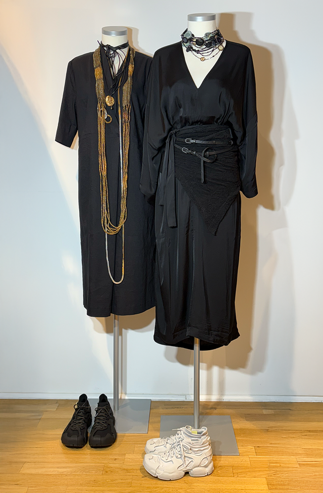 Zwei elegante schwarze Damenmäntel mit Accessoires und passendem Schuhwerk auf Mannequins.