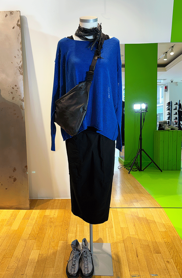 Modell auf Mannequin mit blauem Langarm-Shirt, schwarzem Rock und Lederbeutel, graue Schuhe.