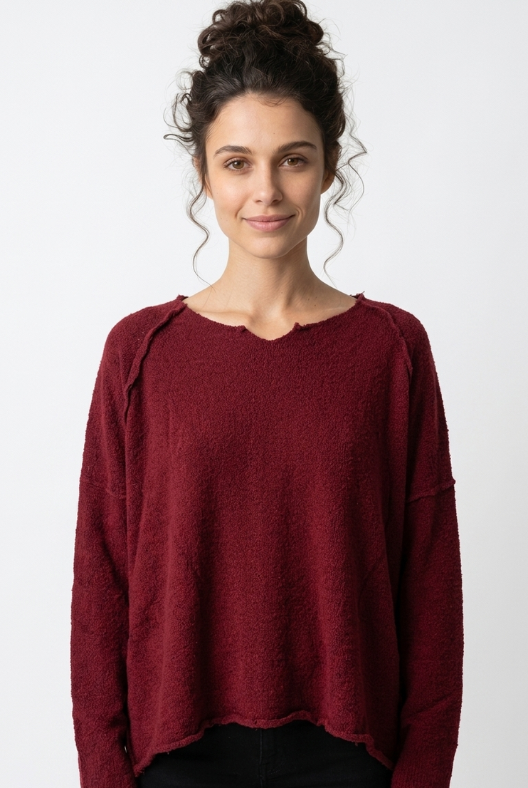 Frau trägt burgunderfarbenen oversized Pullover mit hochgestecktem Haar, lächelt freundlich.