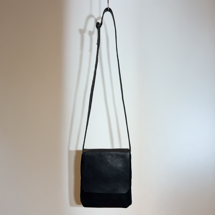 Schwarze Leder-Mini-Tasche mit kurzem Henkel an hellen Wand.